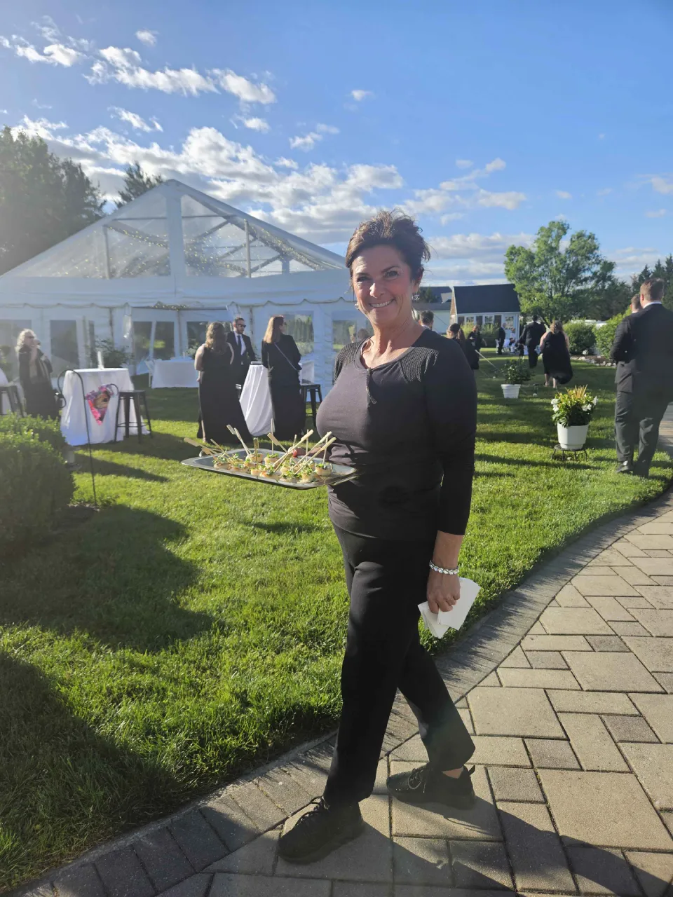 Professional server carrying a tray of passed appetizers at an outdoor tented cocktail party