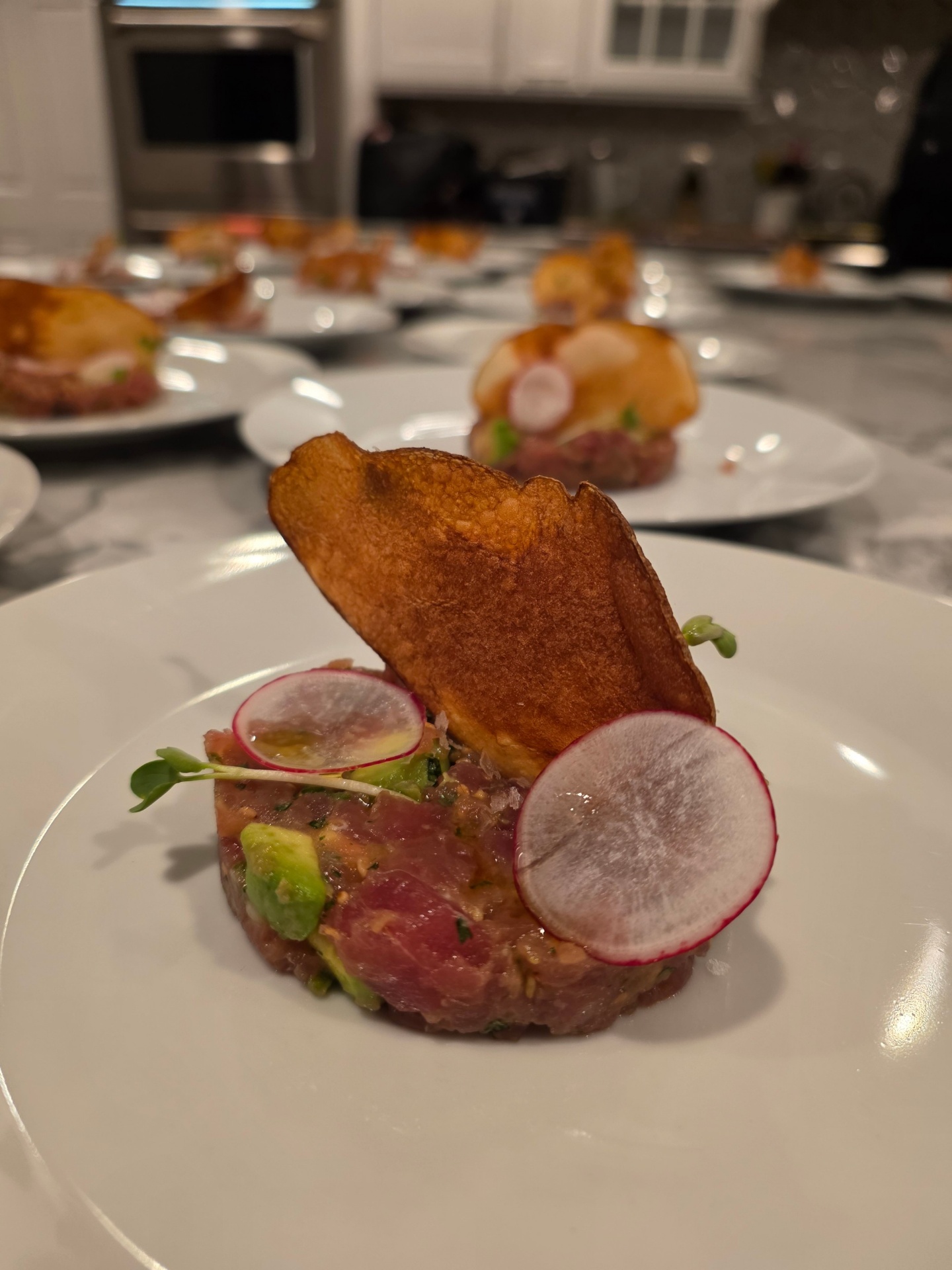 Tuna tartare with avocado and shaved radish plated over a marble chef's table for a private dinner party