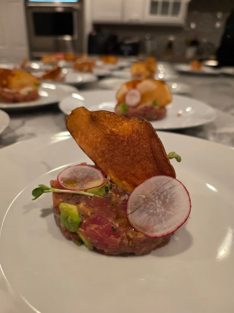 Tuna tartare with avocado and shaved radish plated over a marble chef's table for a private dinner party